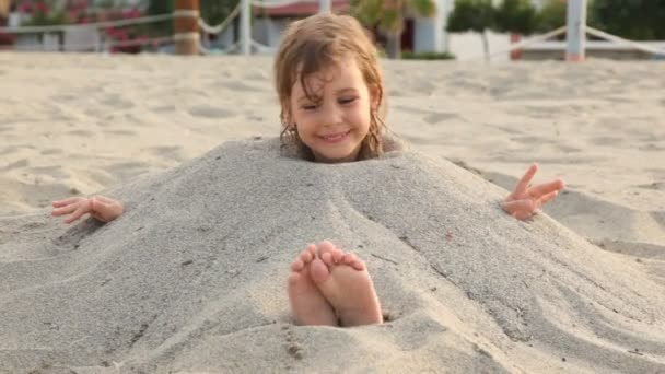 Liten flicka leenden lokalisering fylld med sand på halsen på stranden — Stockvideo