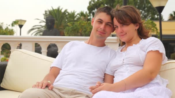 Paar liefhebbers ziet er in elkaar gezicht met glimlach die op de bank zit — Stockvideo
