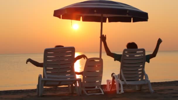 Parents and daughter are sitting on chaise-longue on beach — Stock Video