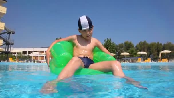 Boy sitting on inflatable chair in the pool water — Stock Video