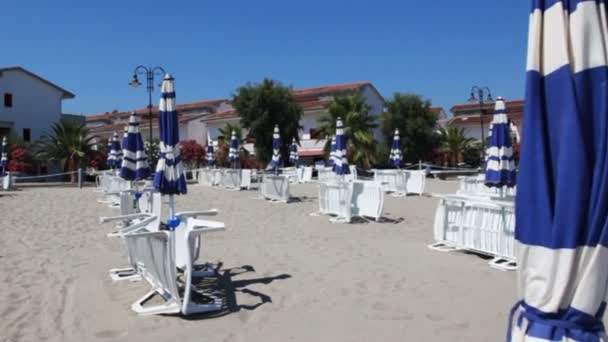 Beach near town with downcast umbrellas and sunbeds — Stock Video