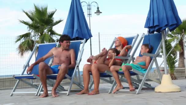 Pais e filhos estão sentados em cadeiras de praia e conversando — Vídeo de Stock