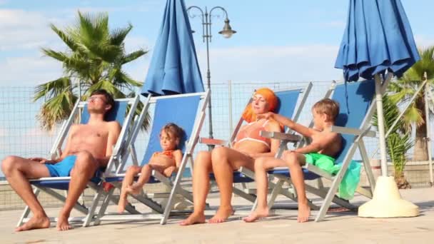 Pais e filhos estão sentados em cadeiras de praia e parados de brincar às mãos — Vídeo de Stock