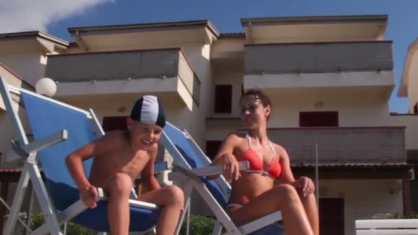 Mother and son sitting in deckchairs, then boy jumps to pool water — Stock Video