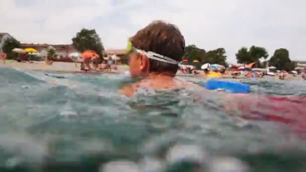 Jongen zwemt in zee naar de wal, dan camera schiet hem onder water — Stockvideo