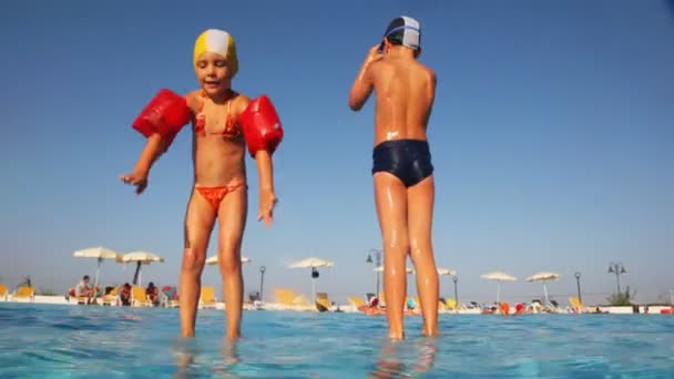 Petite fille avec garçon debout sur la section piscines et à tour de rôle sauter — Video