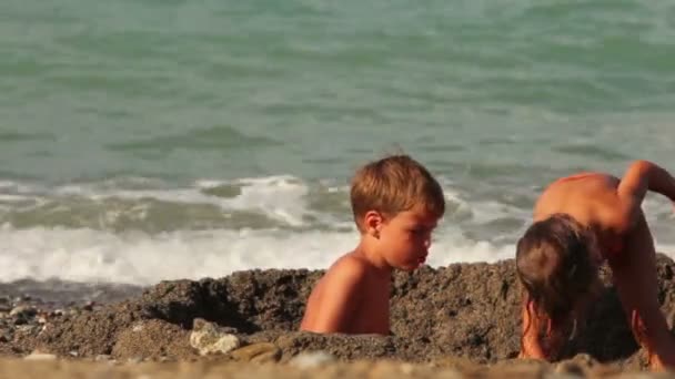 Двое детей находятся в маленькой яме в песке перед водой — стоковое видео