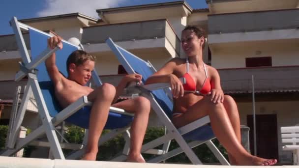 Mother and her son sitting in deckchairs at pool edge — Stock Video