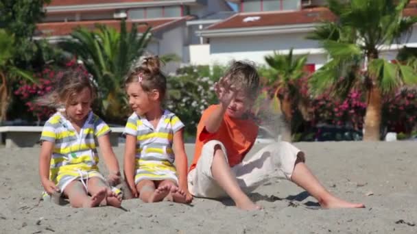 Dvě děti, které sedí na písku a házet je proti domu — Stock video