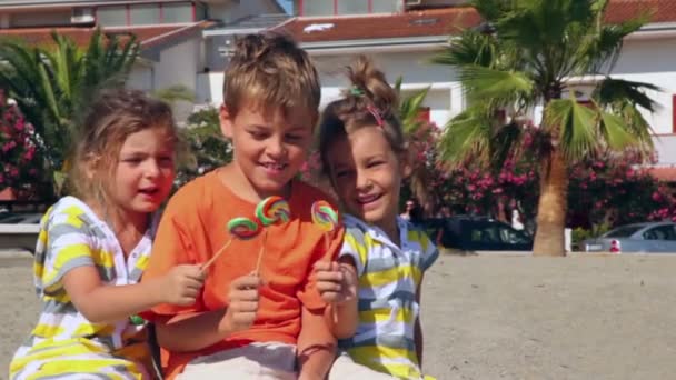 Albero bambini seduti sulla sabbia e mostrando caramelle lolly l'un l'altro — Video Stock