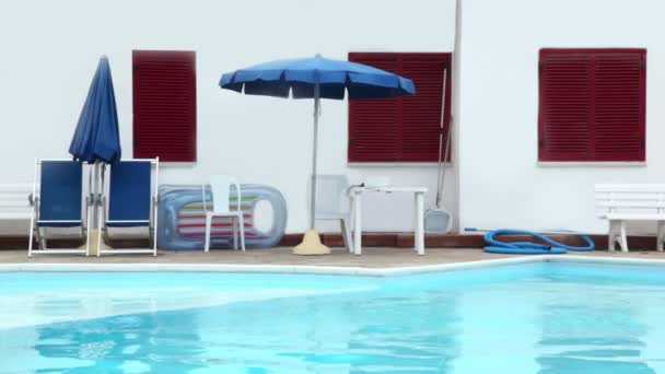 Parasols, stoelen en andere dingen zijn op de rand van het zwembad — Stockvideo