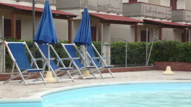 Mehrere Liegestühle mit Blick auf den Pool vor der Kulisse eines Hotels — Stockvideo