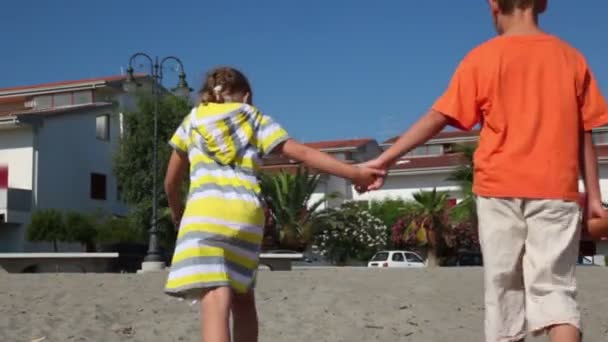 Tree kids boy and two girls going from sea by sand street — Stock Video