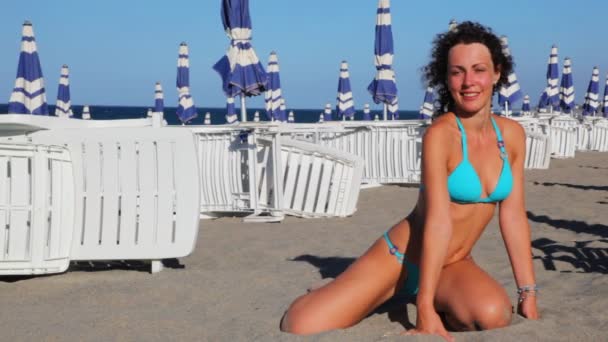 Женщина стоит на коленях на песке на пляже — стоковое видео