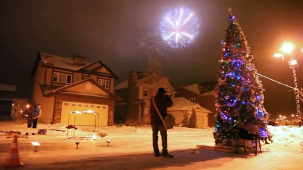 Fyrverkeri i himlen under ett möte med nyår, gatan där är hög fir-julgran — Stockvideo