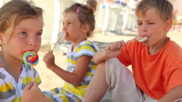 Tres niños sentados en la arena y comiendo dulces — Vídeo de stock