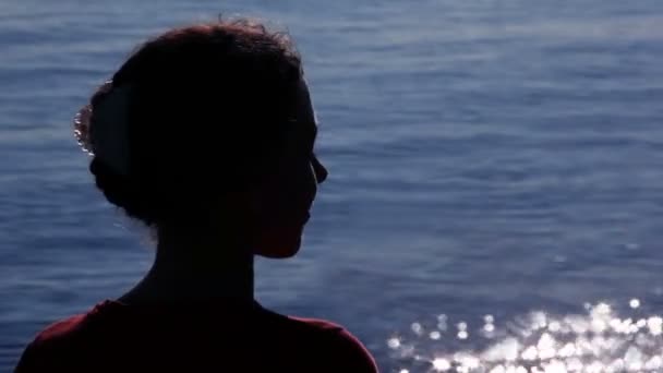 Силуэт женщины повернул голову с солнечными узорами на воде позади — стоковое видео