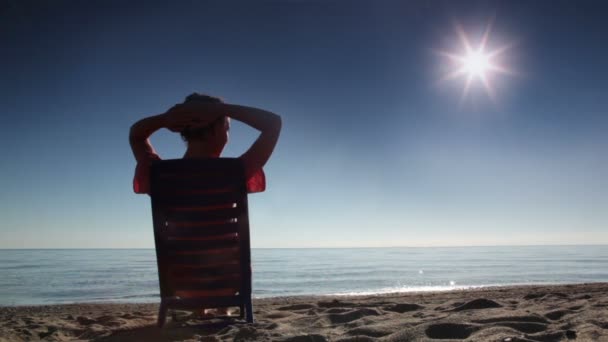 Woman sitting on deckchair and tans holding hand behind head — Stock Video