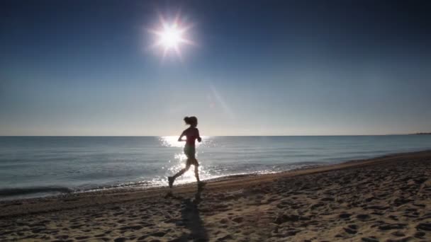 Молодая женщина бежит вдоль пляжа возле морской воды — стоковое видео