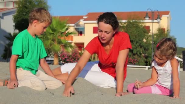 Mor och hennes barn som sitter på sand, gjorde sand högen — Stockvideo