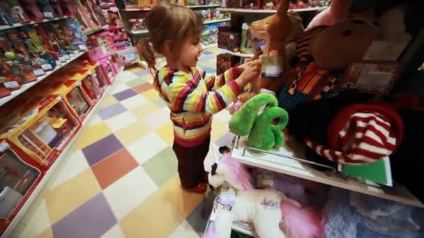 Niña elegir cuidadosamente juguete en la tienda — Vídeo de stock