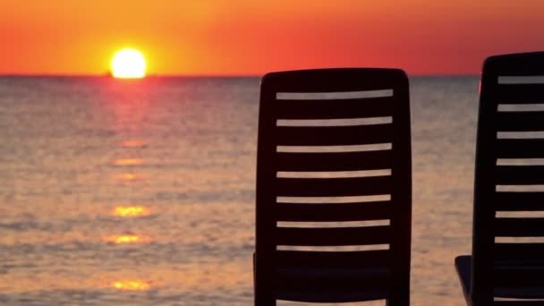 Zeegezicht bij avond zonsondergang getoond achter twee ligstoelen — Stockvideo