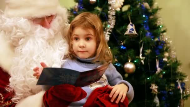 Menina lê com Papai Noel na frente da árvore Vídeos De Bancos De Imagens Sem Royalties