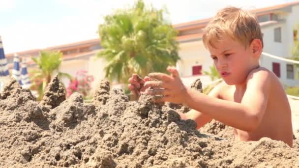 Мальчик сидит и строит замок из песка — стоковое видео
