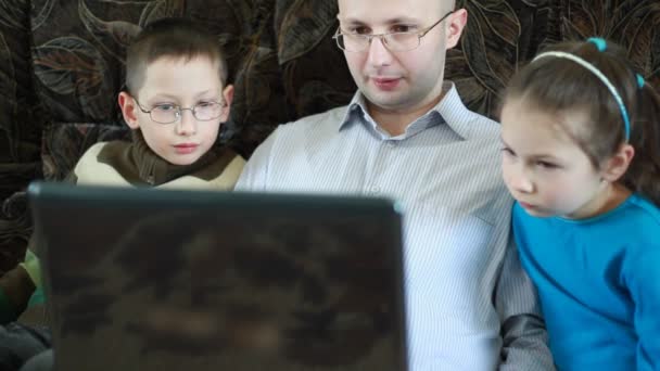 Padre lavora sul computer portatile seduto accanto a suo figlio e sua figlia — Video Stock