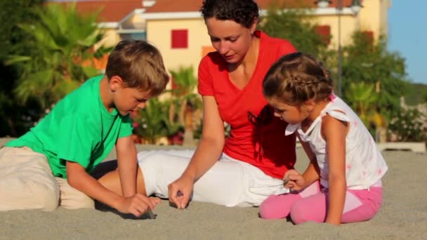 Madre y sus hijos sentados en la arena y escribiendo en ella — Vídeos de Stock