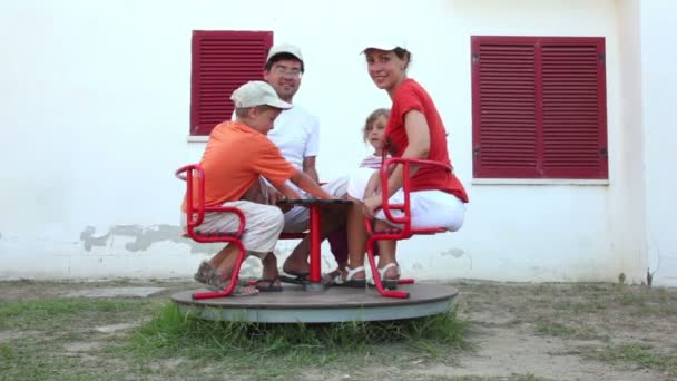 Ouders en kinderen zittend op een carrousel, en beginnen om te roteren — Stockvideo