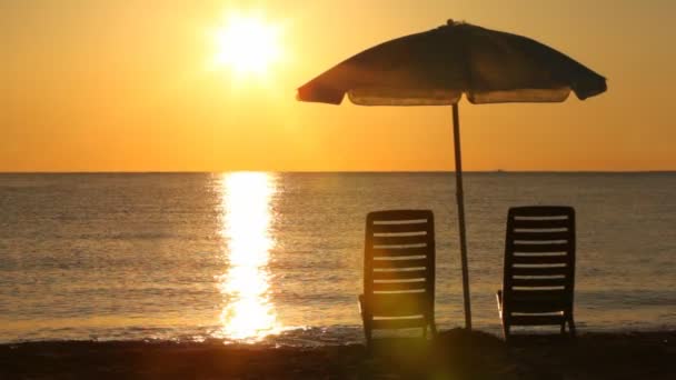 Zwei Liegestühle stehen abends am Strand unter Sonnenschirm — Stockvideo