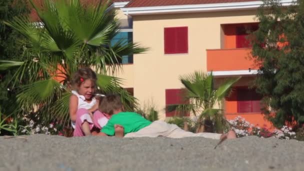 Двое детей играют на песке, они борются — стоковое видео