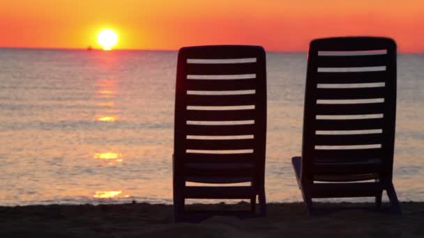 Twee ligstoelen staan op strand vissen boot zeilen op horizon — Stockvideo