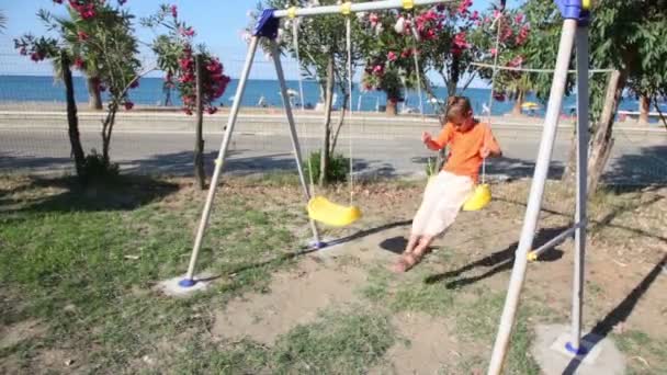 Jongen swingen op een schommel tegen de achtergrond van het strand — Stockvideo