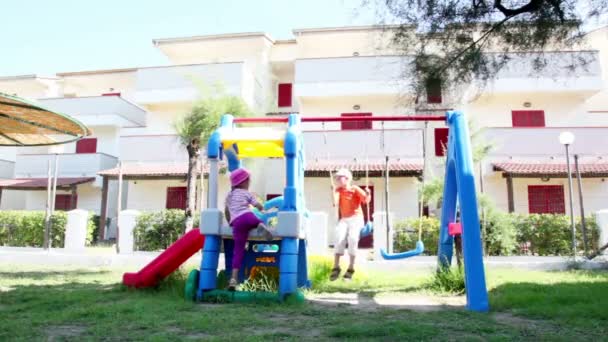 Twee kinderen op de speelplaats, jongen is slingerbewegingen op schommel meisje ging — Stockvideo