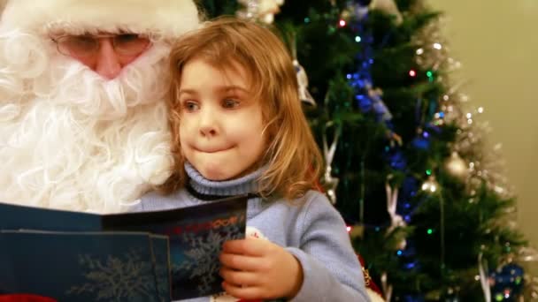 Chica sentada en Santa Claus arrodillada frente al árbol — Vídeos de Stock