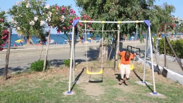 Boy swinging on a swing against the backdrop of the beach — Stock Video