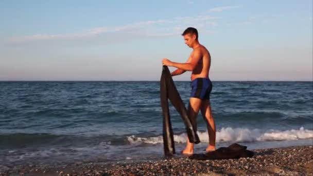 Człowiek stojący na plaży i mycia komplet spodnie w morze — Wideo stockowe