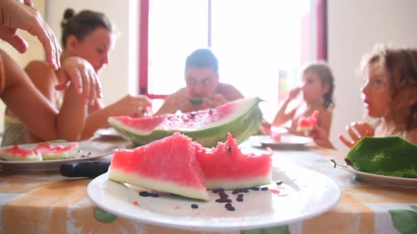 Skivad vattenmelon på plattan och familj runt bordet äter det — Stockvideo