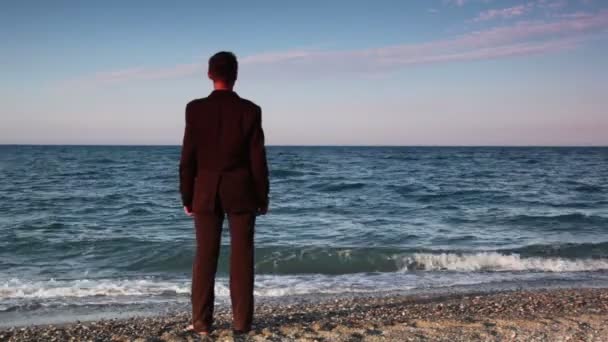 Hombre de traje de pie sobre guijarros de playa — Vídeos de Stock