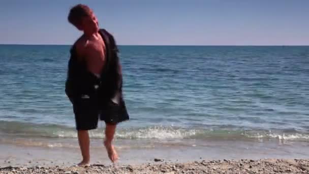 Boy going out sea water and put off suit jacket — Stock Video