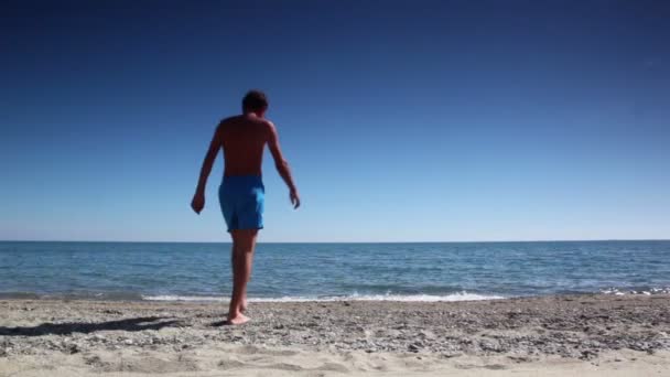 Hombre caminar por la playa arena al agua y luego volver — Vídeos de Stock