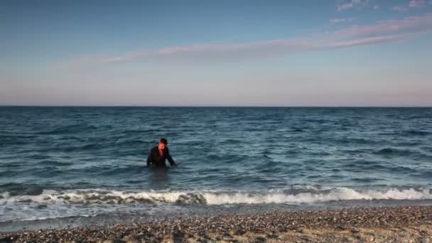 Человек в мокром костюме выходит из морской воды — стоковое видео