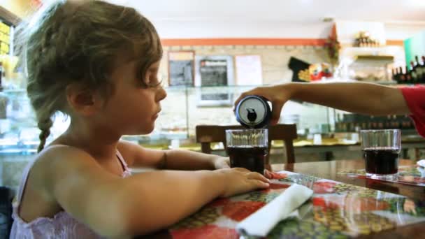 Маленькая девочка сидит за столом, а мальчик наливает воду в стаканы. — стоковое видео
