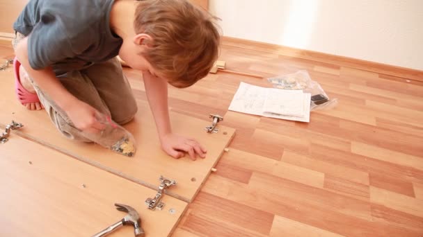 Little boy construct piece of wooden furniture on floor — Stock Video