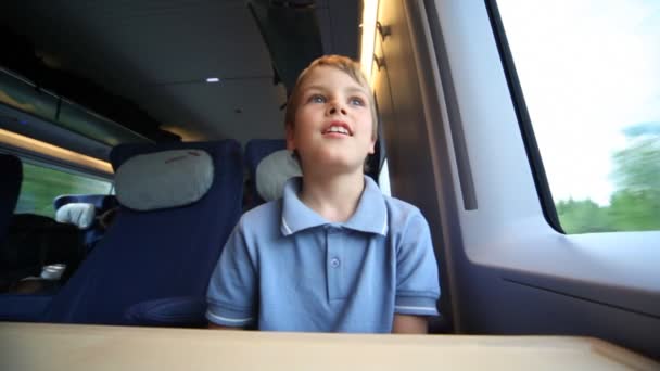 Lachende jongen zit en kijkt uit venster trein tijdens beweging — Stockvideo