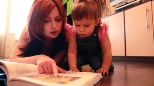 Mamma e bambina sono sdraiati sul pavimento considerando libro — Video Stock