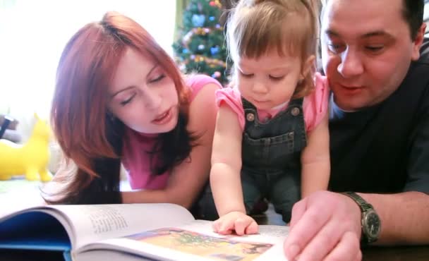 Los padres y la niña están tirados en el piso buscando libro — Vídeo de stock