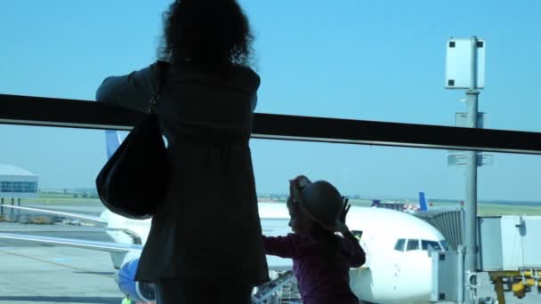 Silhouetten van vrouw met dochter kijken via venster op vliegtuigen op luchthaven — Stockvideo